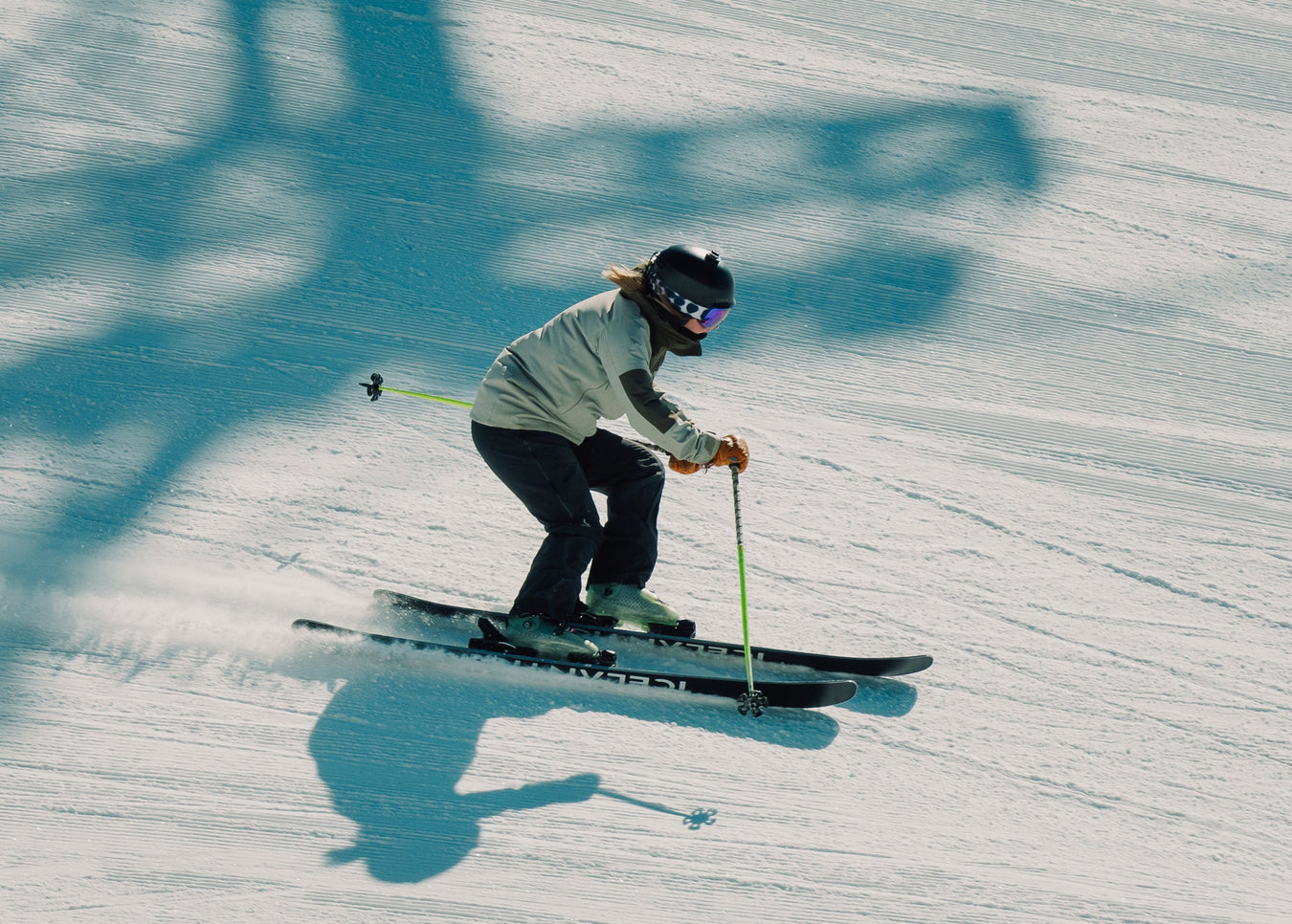 A person in a red jacket and white pants stands in snow at dusk, holding skis and ski poles, with a headlamp shining brightly.