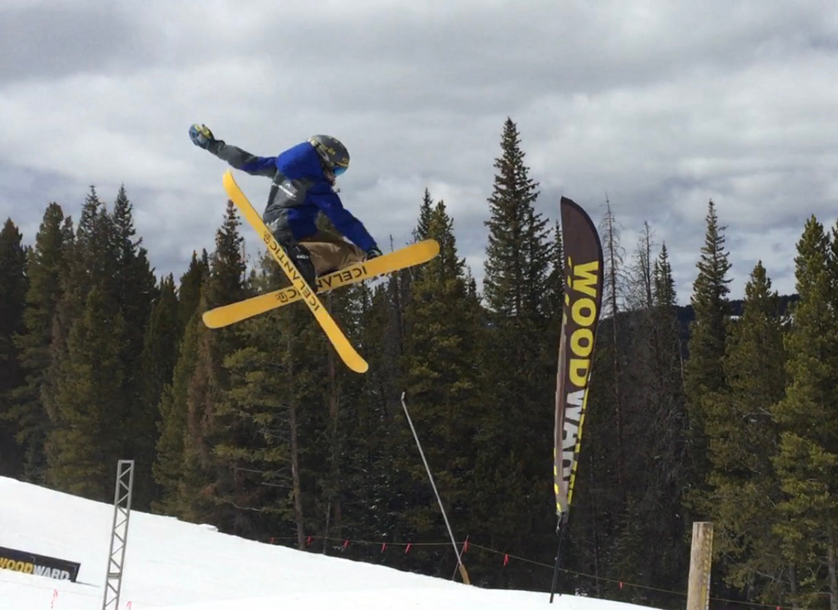 Two skiers in bright outfits descend snowy, tree-lined slopes on a sunny day. The left skier navigates between trees, while the right skier moves down an open, steep run. Illustration of a skier between images.