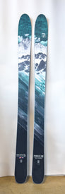 A pair of Icelantic Demo - 23/24 Pioneer 109 skis, showcasing teal and white mountain graphics with snow-covered peaks and geometric patterns, is displayed upright against a plain background. Handmade in Colorado.