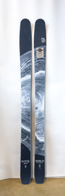A pair of black Icelantic Demo - 23/24 Natural 101 skis featuring a distinctive white tree ring pattern stand upright against a white background. The skis display the "Natural 101" label along with small logos and text near the tips and tails. Handmade in Colorado, these lightweight skis are designed for backcountry touring, seamlessly blending top-notch performance with artisanal craftsmanship.