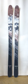 A pair of Icelantic Demo - 23/24 Pioneer 86 skis featuring a mountain landscape graphic with snow-capped peaks and geometric patterns. The all-mountain skis stand upright against a white background, showcasing the craftsmanship of handmade in Colorado design.