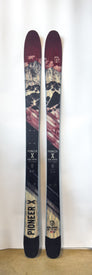 A pair of Icelantic Demo - 23/24 Pioneer X all-mountain skis featuring a mountain landscape design in red, black, and beige tones, standing upright against a white background.