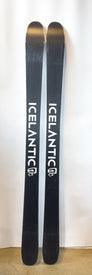A pair of Demo - 23/24 Pioneer 96 skis by Icelantic, featuring a black design with white branding, stand upright against a white background on a concrete floor, highlighting their versatile all-mountain performance.