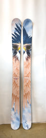A pair of Demo - 23/24 Maiden 111 women’s freeride skis by Icelantic stand upright against a white background, each ski displaying a vivid bird of prey face and wing graphic that together form a striking eagle image—built to perform as exceptional powder skis.