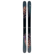 A pair of Icelantic Skis Torrent 102, black with intricate pine cone graphics in brown and purple hues, stand vertically side by side on a white background.