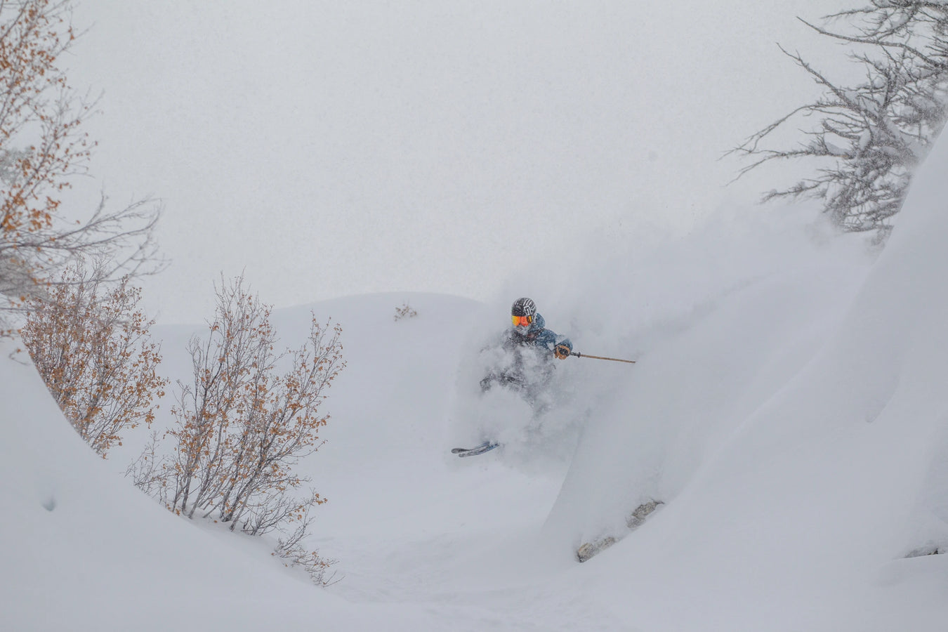 Clad in a helmet and goggles, a skier effortlessly glides through deep powder on Icelantic Skis’ Nomad 112, weaving between snow-laden trees on a cloudy winter day.