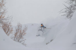 Clad in a helmet and goggles, a skier effortlessly glides through deep powder on Icelantic Skis’ Nomad 112, weaving between snow-laden trees on a cloudy winter day.
