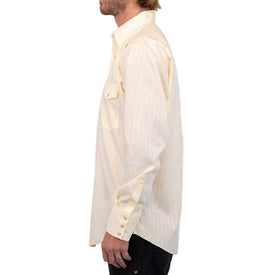 A man with light brown hair, shown in profile against a white background, wears a cream-colored Wrangler Agave Pearl Snap Shirt by Icelantic Skis featuring thin vertical stripes and long sleeves.