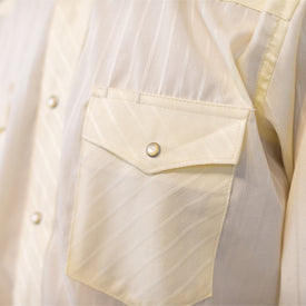 Close-up of the Wrangler Agave Pearl Snap Shirt by Icelantic Skis, featuring a cream-colored fabric with a subtle striped and diamond pattern. This cowboy dress shirt includes a chest pocket and classic pearl snap buttons, adding textured detail reminiscent of traditional western wear.