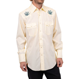 A man wearing the Wrangler Agave Pearl Snap Shirt by Icelantic Skis—a cream-colored, long-sleeve western shirt featuring two front pockets and green agave plant embroidery on the shoulders.