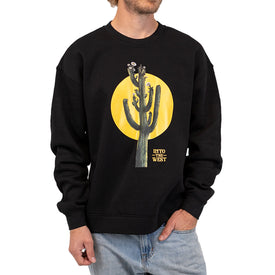 A person is wearing the Cactus Crew, a unisex crewneck sweatshirt by Icelantic Skis made from recycled polyester fleece. The black sweatshirt showcases a cactus graphic with a yellow sun in the background and features the text "Into the West" printed near the base of the cactus. The outfit is finished with light blue jeans.