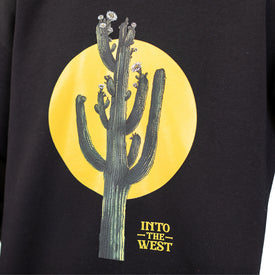 Illustration of a cactus adorned with small white flowers set against a large yellow circle, with "INTO THE WEST" printed below on a black background. Inspired by the adventurous spirit of the Nomad 106 crew, this design is featured on the Cactus Crew unisex crewneck sweatshirt by Icelantic Skis, made from recycled polyester fleece.