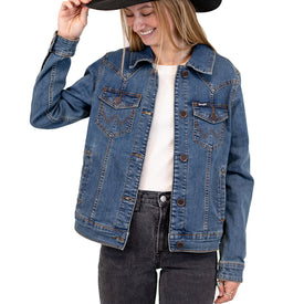 A woman wearing the Icelantic Skis Wrangler Cactus Denim Jacket and black jeans smiles while holding a wide-brimmed hat, standing against a white background.