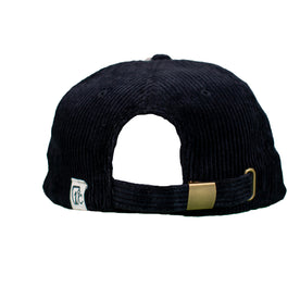 The Cowgirl Ski Club Corduroy Cap - Black by Icelantic Skis is shown from the back, highlighting its adjustable gold buckle strap and a small white fabric tag with text on the left side. This classic six-panel hat effortlessly adds Cowgirl Ski Club flair to any laid-back look.