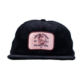 The Cowgirl Ski Club Corduroy Cap - Black by Icelantic Skis is a six-panel black corduroy cap, featuring a pink patch that reads "Cowgirl Ski Club 2024 Icelantic Skis" along with an illustration of a cowgirl on skis.