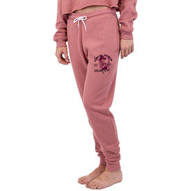 A person is standing barefoot wearing the Icelantic Skis Cowgirl Ski Club Joggers in pink, featuring a drawstring waist and "ICELANDIC" graphic on the left thigh. Their matching sweatshirt and cropped head give off relaxed lounge pants vibes from the Cowgirl Ski Club collection.