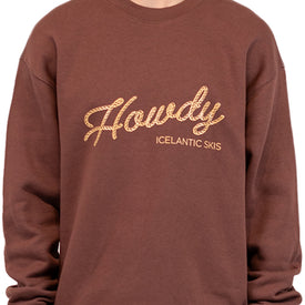 A person wears the Icelantic Skis Howdy Crew, a unisex pullover in brown featuring “Howdy” in cursive rope-style lettering with the ICELANTIC SKIS logo below, made from cozy recycled polyester sweater fabric.