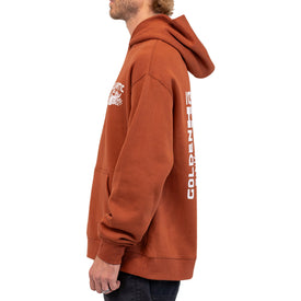 A person wearing a brown Mezcal Skull Hoodie by Icelantic Skis, featuring white graphics and text on the chest and sleeve, stands sideways against a white background. This unisex oversized hoodie is perfect for a casual, modern look.