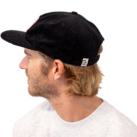 A man with blonde hair, wearing the Icelantic Skis Cowgirl Ski Club Corduroy Cap in black and a light gray sweatshirt, is looking to the left.