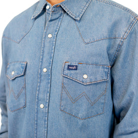 A person wearing an Icelantic Skis Wrangler Rattlesnake Denim Shirt, which features two front chest pockets with flap closures and decorative stitching, along with a small Wrangler logo tag on the left pocket.