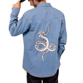 Wearing the Wrangler Rattlesnake Denim Shirt by Icelantic Skis, a person with their back to the camera adjusts their hat, showcasing the bold black-and-white Nomad 94 snake design on the shirt.