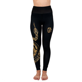 A person wearing Icelantic Skis Rattlesnake Leggings, crafted from Hyper Wiking WIKMAX Fabric and featuring a gold snake design with a gold logo on the left thigh, is standing barefoot against a white background.