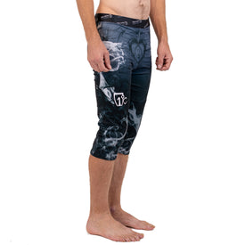 A barefoot person stands sideways wearing black and white smoke-patterned Astronaut Wikmax Baselayer 3/4 Bottom athletic compression pants by Icelantic Skis, made with WIKMAX fabric and reaching mid-calf. Their hands are relaxed at their sides, and they are not wearing a shirt. The background is plain white.
