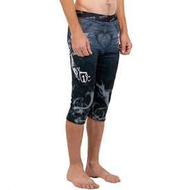 A person stands barefoot wearing Icelantic Skis Astronaut Wikmax Baselayer 3/4 Bottoms—black and gray grappling spats featuring a white design on the left thigh—shown from mid-torso to feet, facing slightly left against a white background.