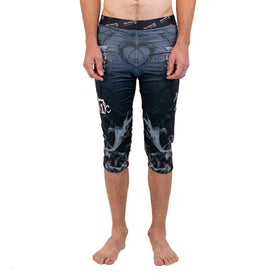 A person stands barefoot, wearing the Icelantic Skis Astronaut Wikmax Baselayer 3/4 Bottom, which features a black and gray smoky pattern with a heart design on the front. Their arms are relaxed by their sides.