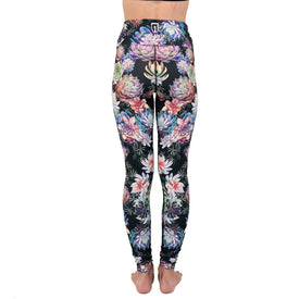 A person stands barefoot facing away, wearing Icelantic Skis' Succulent Leggings—high-waisted black leggings featuring a vibrant floral and succulent print in shades of pink, purple, blue, and green. Crafted from Hyper Wiking WIKMAX Fabric with a supportive high-waist waistband for maximum comfort and a sleek silhouette. The background is plain white.