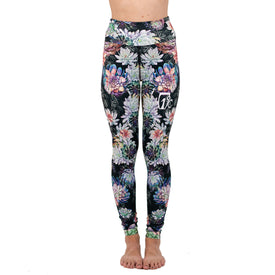 A woman is wearing Icelantic Skis' Succulent Leggings—colorful, floral-patterned leggings with a small white Tz logo on the upper left thigh and a flattering high-waisted waistband—standing barefoot against a white background.