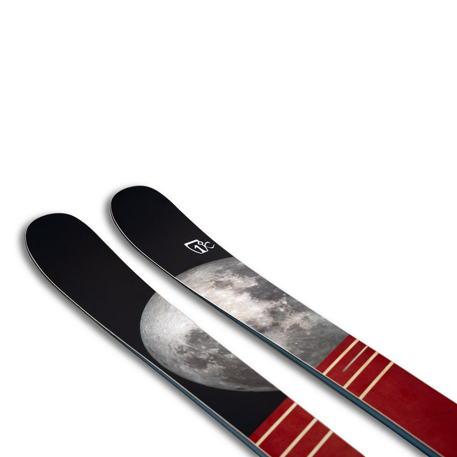 A pair of Icelantic Skis Nomad 100 skis featuring a detailed image of the moon and red stripes on a black background, displayed against a white backdrop.