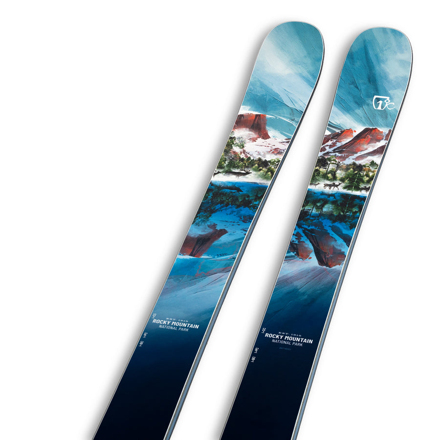 The Icelantic Skis Rocky Mtn NP 100 is a pair of all-mountain skis handmade in Colorado, featuring an artistic mountain landscape design in blue, red, and white tones with the brand’s logo near the tips.