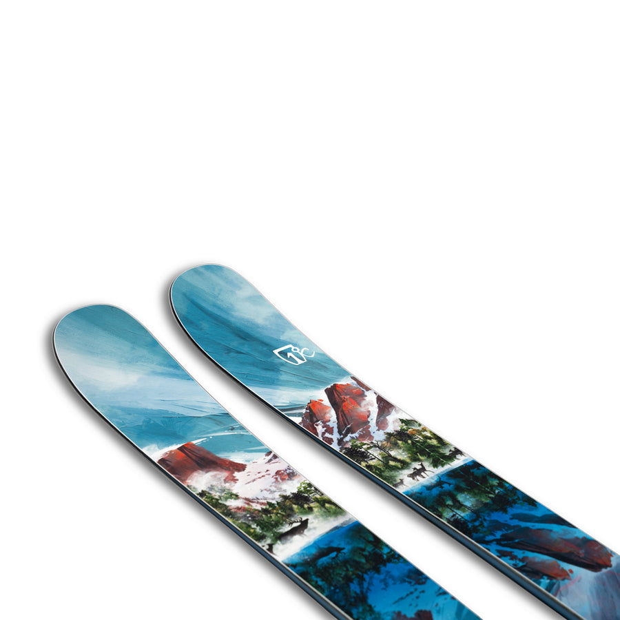 The Icelantic Skis Rocky Mtn NP 100 is a pair of all-mountain skis handmade in Colorado, showcasing a striking blue and white mountain landscape design with trees and red rock formations. These skis combine eye-catching style with outstanding performance, perfect for your next adventure.