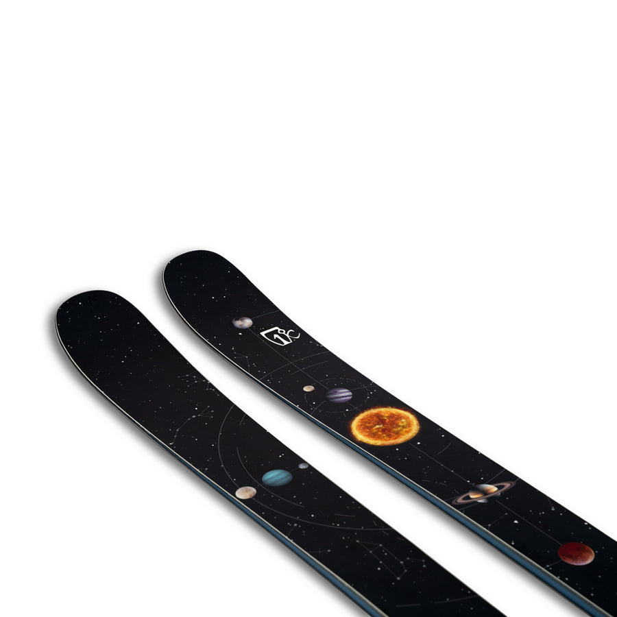 The Icelantic Skis Nomad 94 is a pair of black skis adorned with a space-themed design that features planets, stars, and the sun set against a white background.