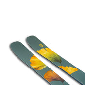 A pair of Icelantic Skis Tempest 100 all-mountain skis in green, highlighted by a yellow and orange flower design near the tips, crafted with a carbon matrix and a poplar and birch wood core, displayed on a white background.