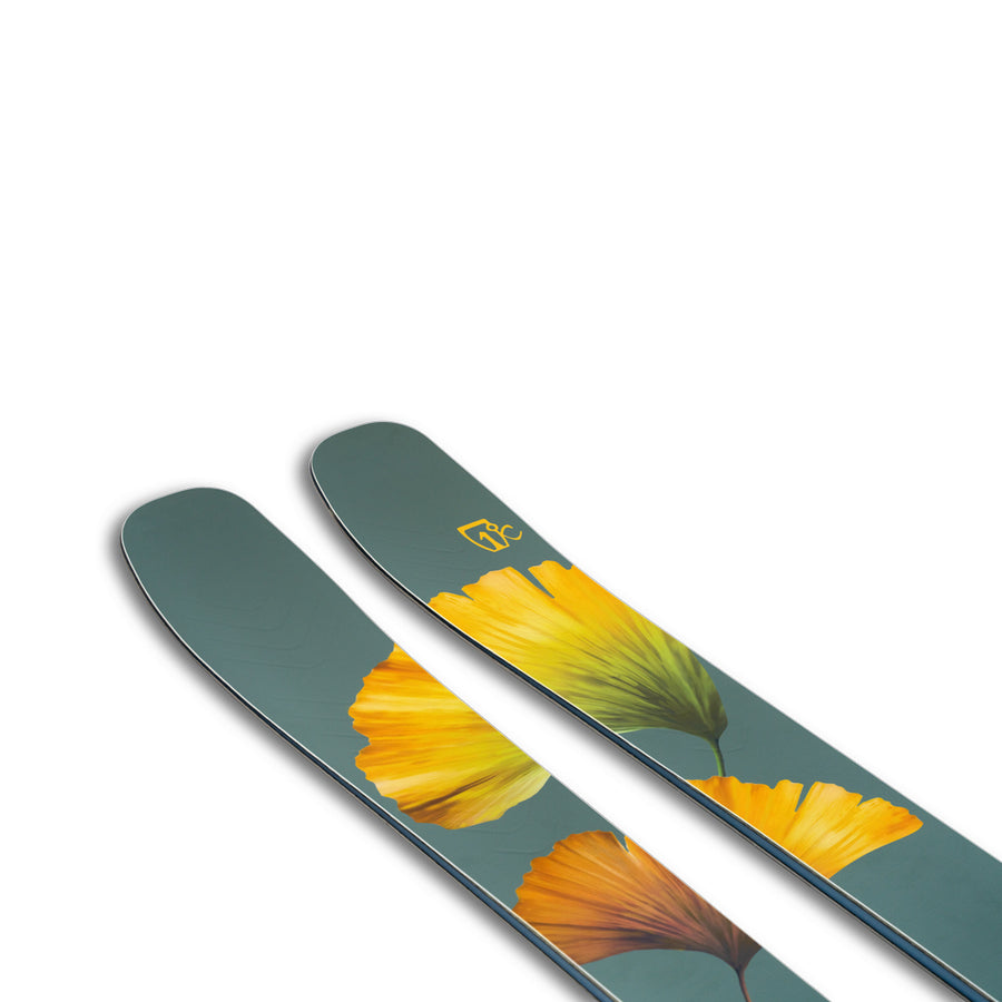 A pair of Icelantic Skis Tempest 100 all-mountain skis in green, highlighted by a yellow and orange flower design near the tips, crafted with a carbon matrix and a poplar and birch wood core, displayed on a white background.