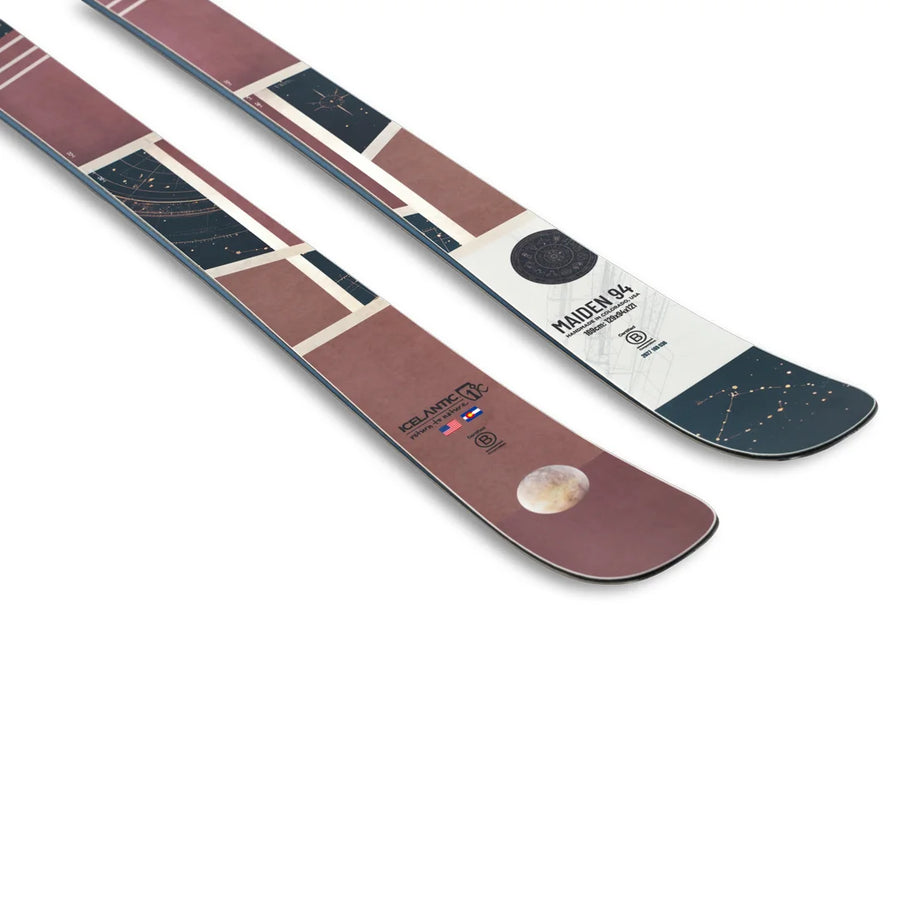 A pair of Icelantic Skis Maiden 94, featuring abstract geometric designs in red, cream, and black hues, adorned with celestial imagery such as a moon and star constellations, and “Maiden 94” text near the tips.