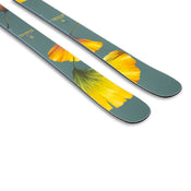 The Icelantic Skis Tempest 100, an all-mountain ski crafted with a poplar and birch wood core, boasts a green base adorned with yellow leaf designs and text near the tips, shown against a white background.