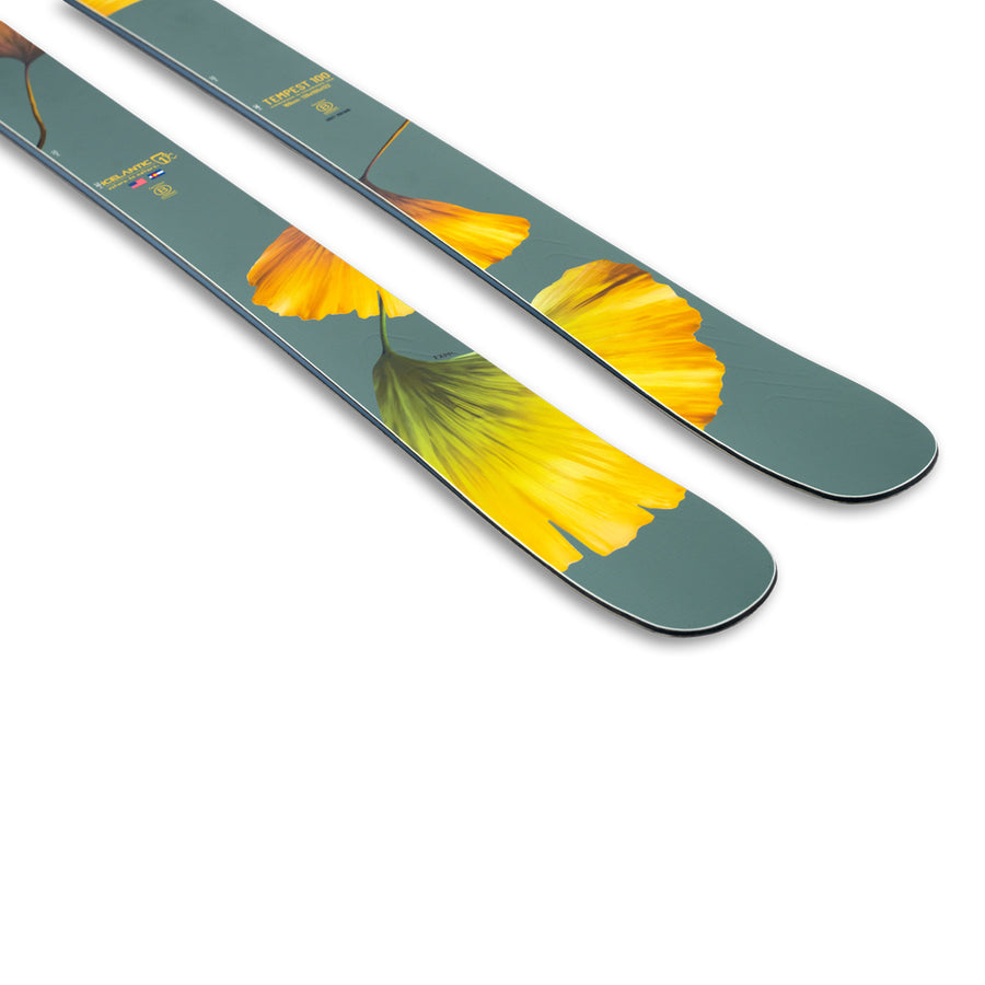 The Icelantic Skis Tempest 100, an all-mountain ski crafted with a poplar and birch wood core, boasts a green base adorned with yellow leaf designs and text near the tips, shown against a white background.