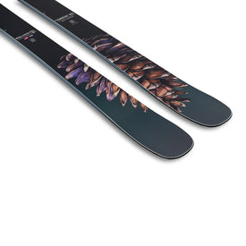 A close-up of two Icelantic Skis Torrent 102 skis, featuring realistic pine cone artwork on their tops, lying parallel on a white background.