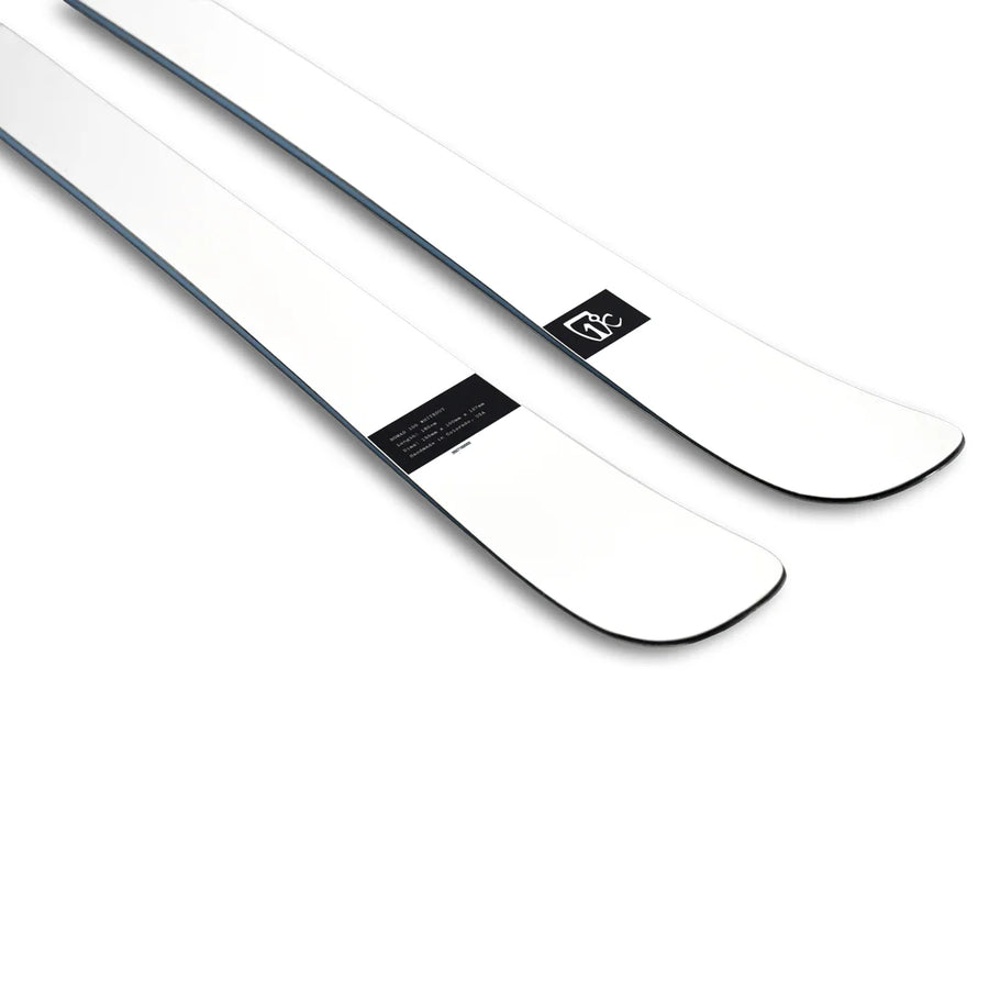 A pair of Icelantic Skis Nomad 100 Whiteout, featuring a sleek white design with black edges and a small black logo near the tips, photographed on a white background.