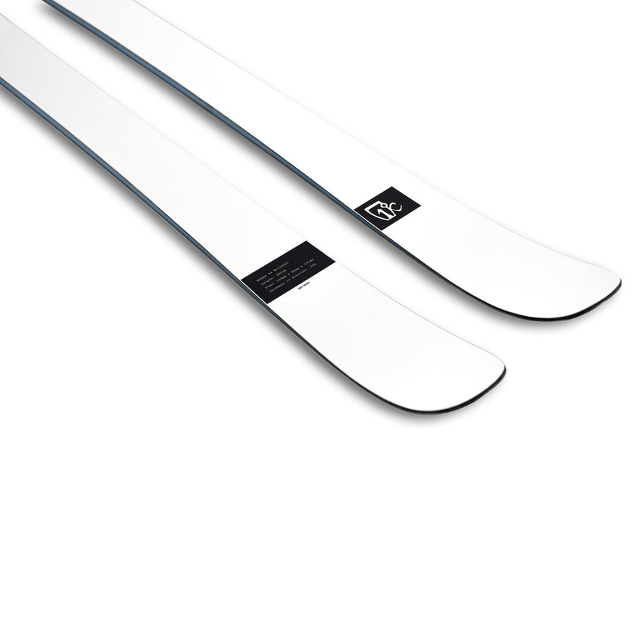 A pair of Icelantic Skis Nomad 94 Whiteout skis in white are shown side by side, featuring slightly upturned tips and a small black label with white text and logo near the front.