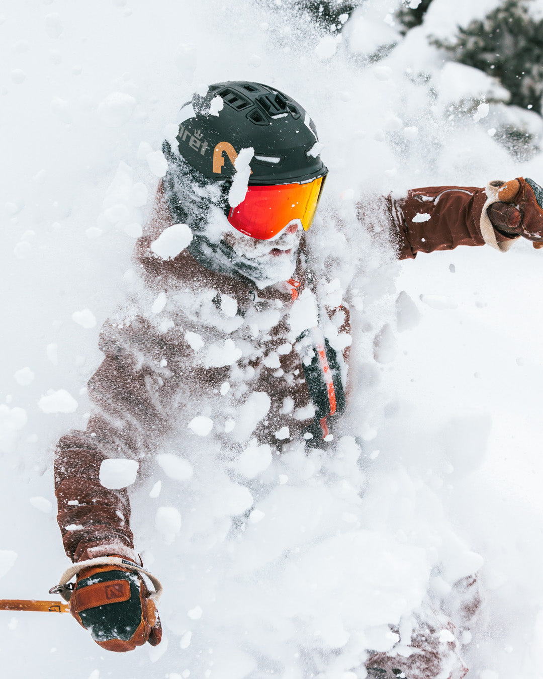 A skier wearing a helmet and goggles is surrounded by a burst of fresh snow, obscuring much of their face and body as they move quickly down a snowy slope.