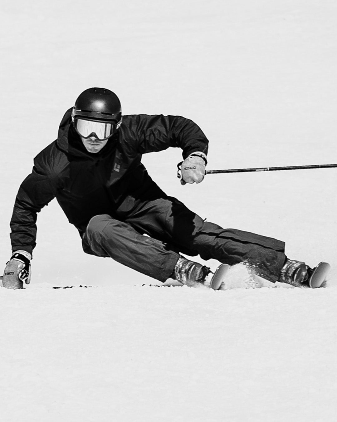 A skier in dark gear and helmet carves sharply on a snowy slope, leaning low to the ground with one hand touching the snow.