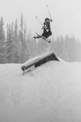 Rider launches off a rail on the Icelantic Skis Nomad 94, executing an aerial trick against a backdrop of snowy trees.
