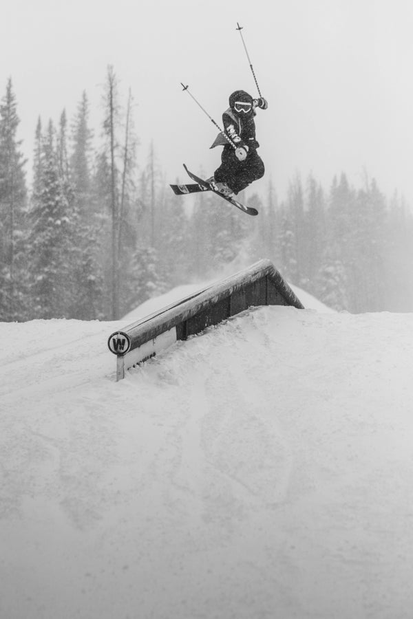 Rider launches off a rail on the Icelantic Skis Nomad 94, executing an aerial trick against a backdrop of snowy trees.
