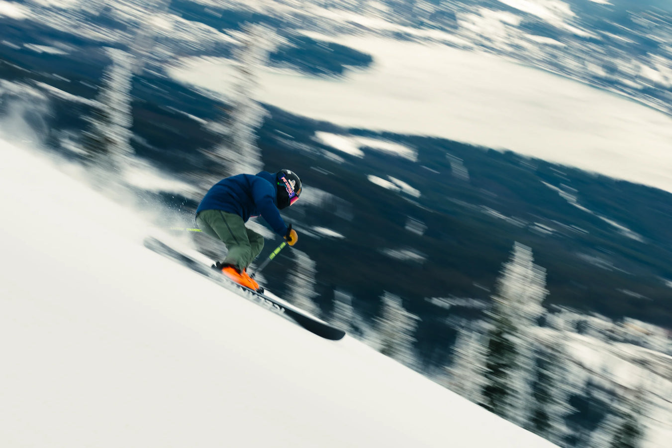 Wearing a blue jacket and helmet, a skier speeds downhill on a snowy slope aboard the Icelantic Skis Torrent 96, with a blurred background of trees and snow emphasizing the dynamic motion.