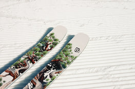 A pair of Icelantic Skis Torrent 96, featuring an intricate tree and branch design, rests on freshly groomed, corduroy-patterned snow.