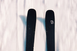 A close-up, top-down view of two black Icelantic Skis Torrent 88 skis on snow, with one ski displaying a white logo near its tip.